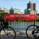 People wearing protective masks walk their bicycles past a social distancing sign reading “KEEP THIS FAR APART” at Jacqueline Kennedy Onassis Reservoir in Central Park during the coronavirus pandemic on May 17, 2020 in New York City.